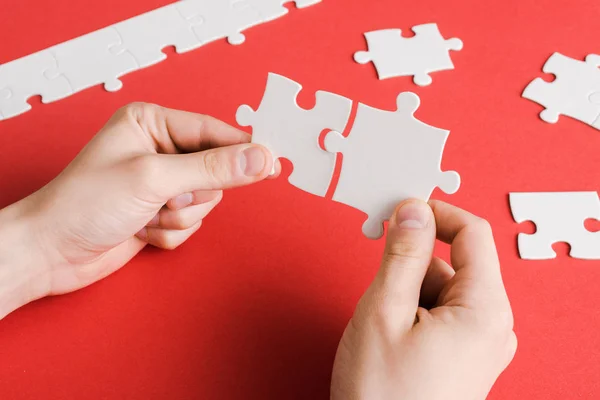 Cropped view of man connecting white puzzle pieces in hands on red — Stock Photo