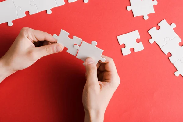 Vue recadrée de l'homme tenant des pièces de puzzle blanc dans les mains sur rouge — Photo de stock