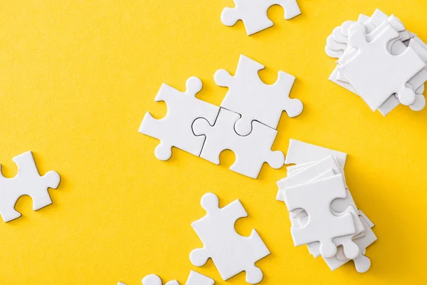 Top view of white stack of jigsaw near connected puzzles isolated on yellow — Stock Photo