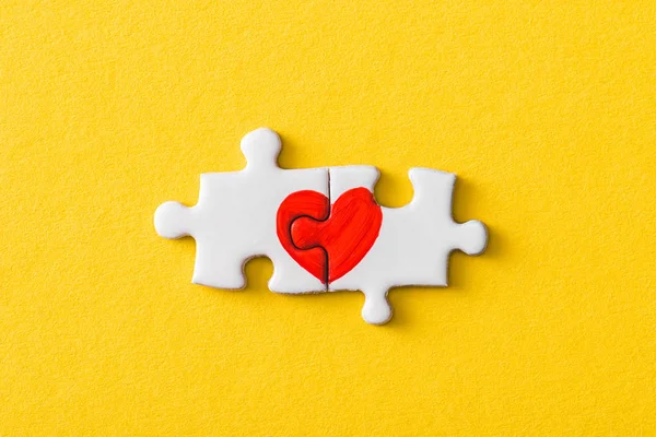 Top view of connected jigsaw puzzle pieces with drawn red heart isolated on yellow — Stock Photo