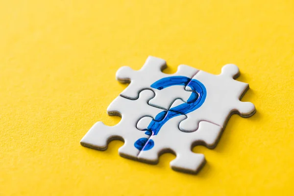 Connected jigsaw puzzle pieces with drawn blue question mark on yellow — Stock Photo
