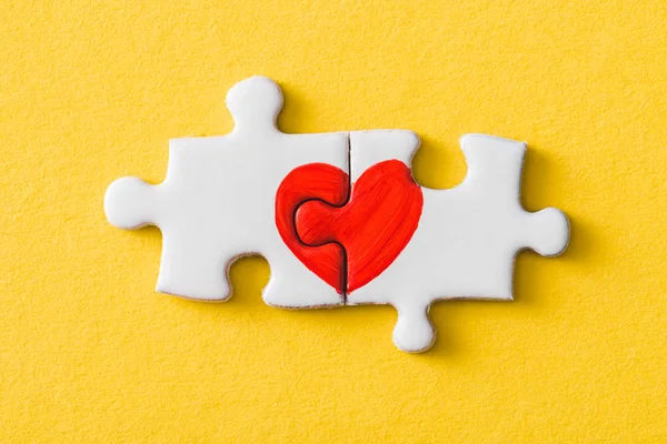 Top view of connected puzzle pieces with drawn red heart isolated on yellow — Stock Photo