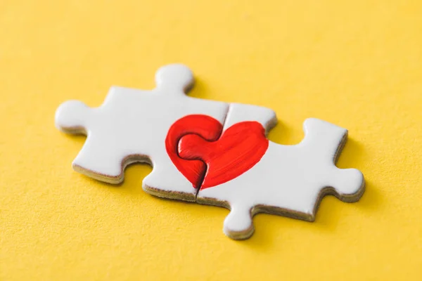 Pièces de puzzle connecté avec coeur rouge dessiné sur jaune — Photo de stock
