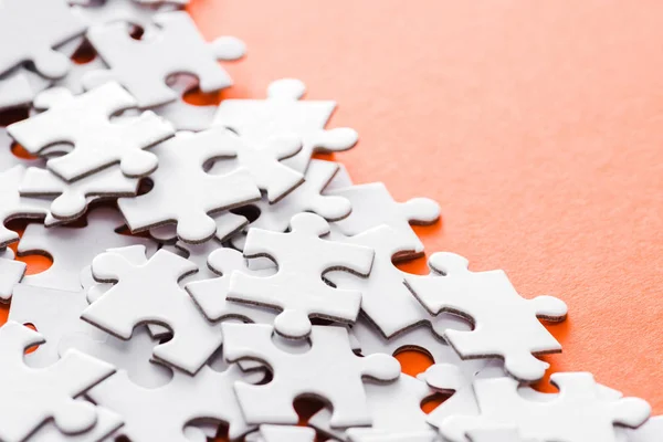 Selective focus of unfinished white jigsaw puzzle pieces on orange — Stock Photo