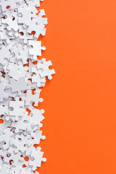 Top view of unfinished white jigsaw puzzle pieces isolated on orange with copy space — Stock Photo