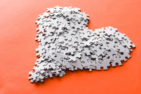 White heart-shaped jigsaw puzzle pieces on orange — Stock Photo