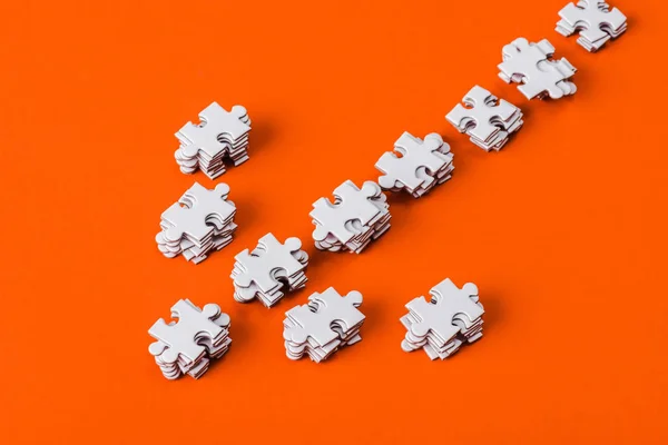 Top view of direction arrow with white jigsaw puzzle pieces on orange — Stock Photo