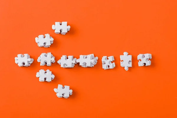 Top view of white direction arrow with jigsaw puzzle pieces on orange — Stock Photo