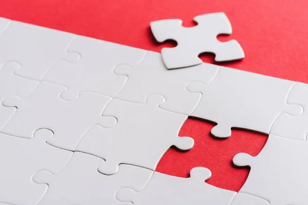 Selektive Fokussierung unvollendeter weißer Puzzles in der Nähe eines separaten, auf rot isolierten Teils — Stockfoto