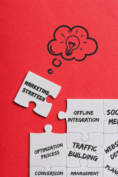 Top view of unfinished white puzzles near separate piece with marketing strategy lettering on red — Stock Photo