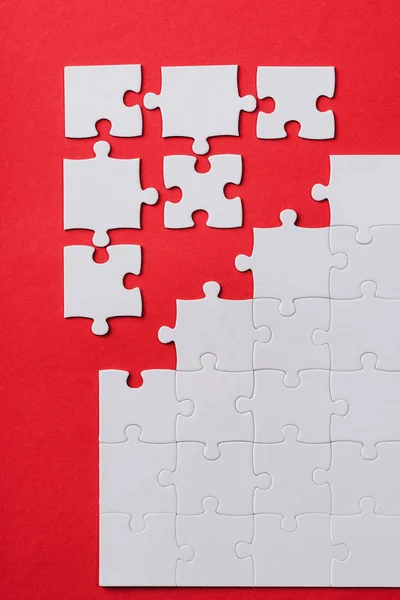 Вид сверху на белые соединенные и отдельные кусочки головоломки, изолированные на красном — стоковое фото