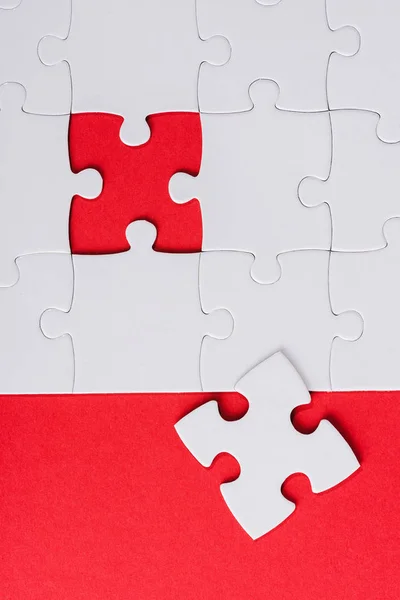 Top view of incomplete white puzzles near separate piece isolated on red — Stock Photo