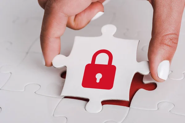 Close up of woman holding white jigsaw with red padlock near connected puzzle pieces — Stock Photo