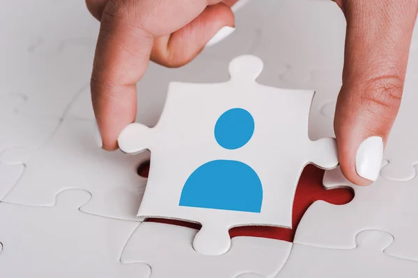 Close up of woman holding white jigsaw with blue human icon near connected puzzle pieces — Stock Photo