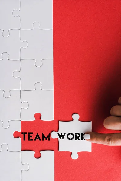 Top view of woman pointing with finger at jigsaw near connected puzzle pieces with teamwork lettering on red — Stock Photo