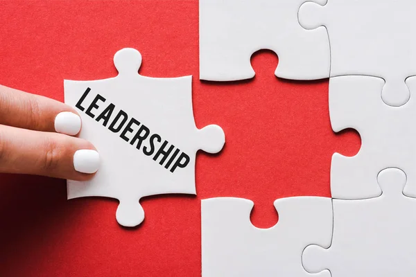 Top view of woman touching jigsaw with leadership lettering near connected white puzzle pieces on red — стоковое фото