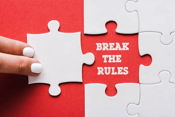 Top view of woman touching jigsaw near break the rules lettering and connected white puzzle pieces and idea lettering on red — стоковое фото