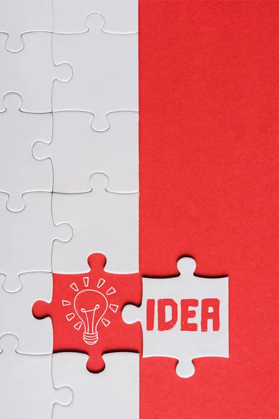 Top view of incomplete jigsaw near white puzzle piece with idea lettering isolated on red — Stock Photo