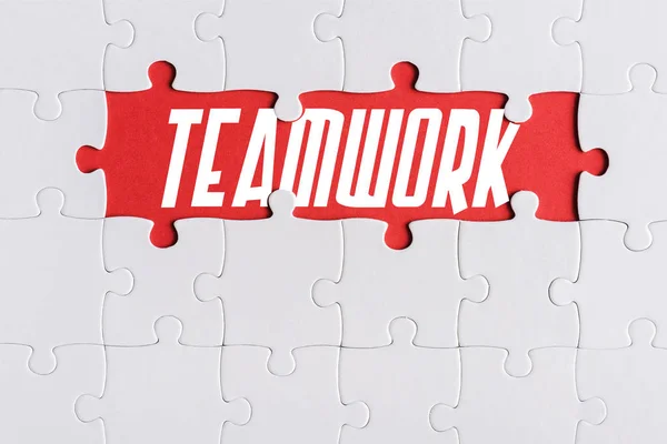 Top view of connected jigsaw puzzle pieces near teamwork letters — Stock Photo