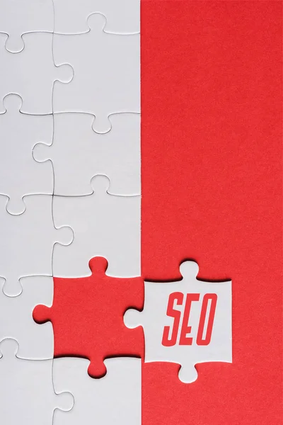 Top view of incomplete jigsaw near white puzzle piece with seo lettering isolated on red — Stock Photo