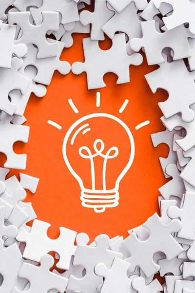 Top view of frame of white jigsaw puzzle pieces around of light bulb lettering on orange — Stock Photo