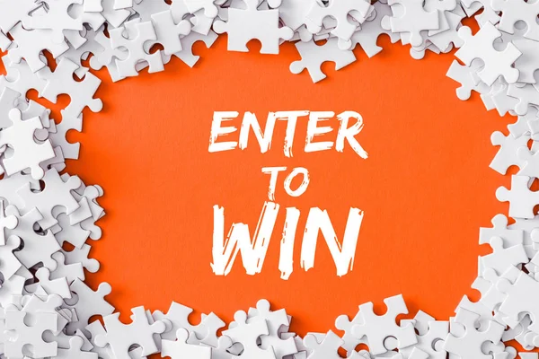 Top view of frame of white jigsaw puzzle pieces around of enter to win lettering on orange — Stock Photo