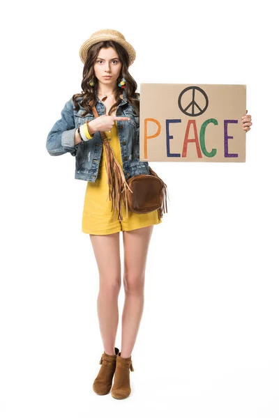 Piena vista lunghezza della ragazza hippie in cappello di paglia che punta con il dito al cartello con iscrizione isolata su bianco — Foto stock