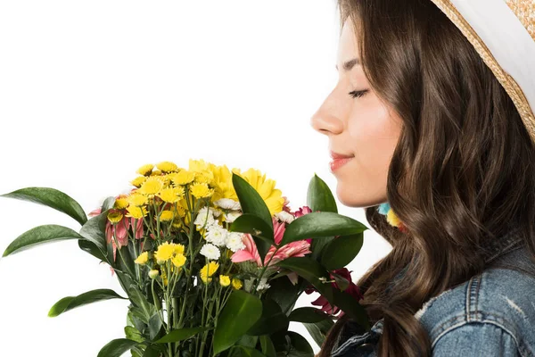 Vista lateral de chica boho en sombrero de paja sosteniendo flores con los ojos cerrados aislados en blanco - foto de stock