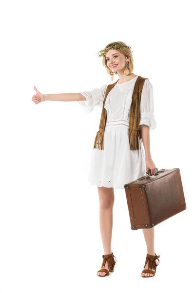 Full length view of smiling boho girl holding suitcase and hitchhiking isolated on white — Stock Photo