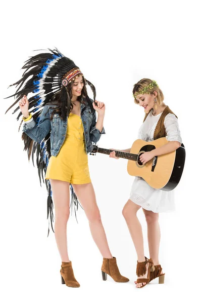 Vista completa de dos chicas hippies bisexuales en tocado indio y corona con guitarra acústica aislada en blanco - foto de stock