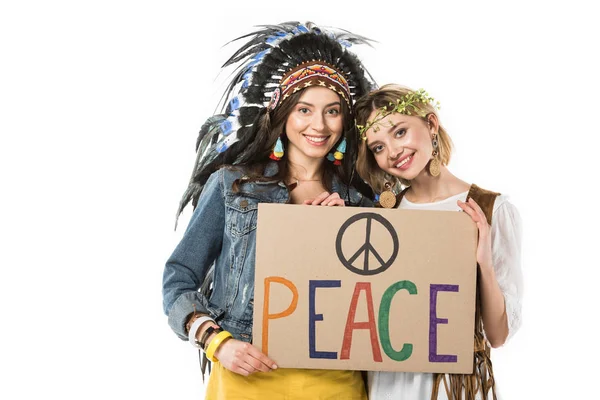 Two bisexual hippie girls in indian headdress and wreath holding placard with inscription isolated on white — Stock Photo