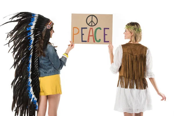 Back view of two bisexual hippie girls in indian headdress and wreath holding placard with inscription isolated on white — Stock Photo