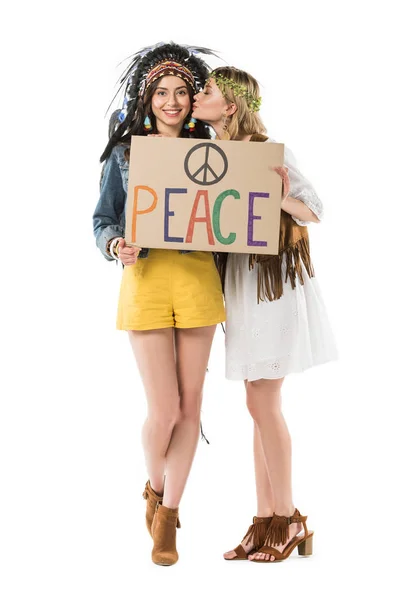 Vue pleine longueur de deux filles hippies bisexuelles en coiffe indienne et couronne tenant une pancarte avec inscription et baiser isolé sur blanc — Photo de stock