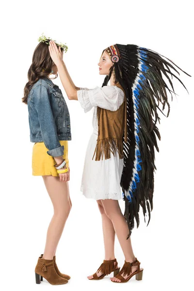 Vista lateral de chica en tocado indio poniendo corona en amigo aislado en blanco - foto de stock