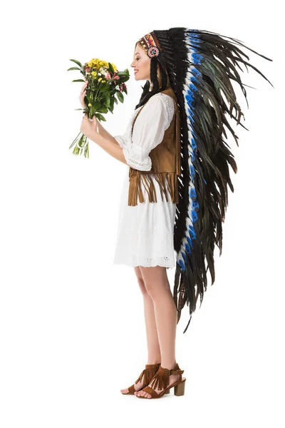 Side view of smiling woman in indian headdress holding flowers isolated on white — Stock Photo