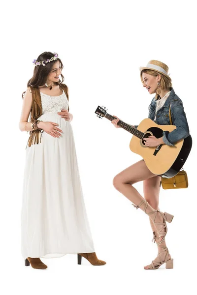 Pleine longueur vue de hippie fille jouer de la guitare acoustique pour petite amie enceinte isolé sur blanc — Photo de stock