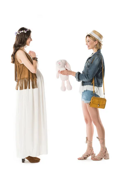 Side view of hippie girl giving toy rabbit to pregnant girlfriend isolated on white — Stock Photo