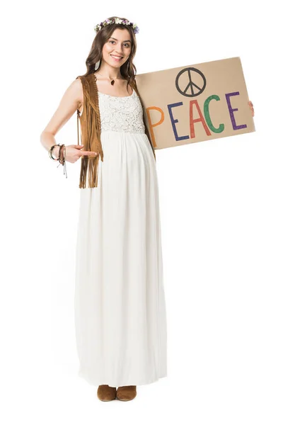 Vista completa de la mujer hippie embarazada señalando con el dedo en el cartel con la inscripción aislada en blanco - foto de stock