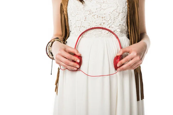 Vue recadrée de femme hippie enceinte tenant des écouteurs sur le ventre isolé sur blanc — Photo de stock