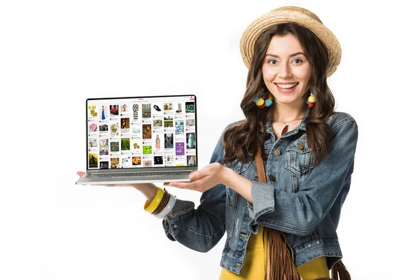KYIV, UCRANIA - 4 DE FEBRERO DE 2019: niña hippie sonriente en sombrero de paja sosteniendo el ordenador portátil con el sitio web de pinterest en la pantalla aislada en blanco - foto de stock