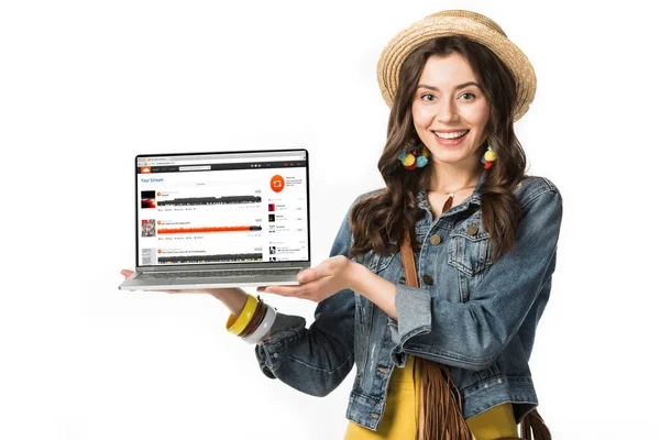 Kyiw, Ukraine - 4. Februar 2019: Lächelndes Hippie-Mädchen mit Strohhut hält Laptop mit Soundcloud-Webseite auf dem Bildschirm isoliert auf weiß — Stockfoto