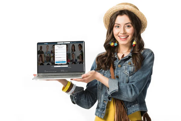 KYIV, UCRAINA - 4 FEBBRAIO 2019: ragazza hippie sorridente in cappello di paglia con laptop in mano con sito web linkedin sullo schermo isolato su bianco — Foto stock