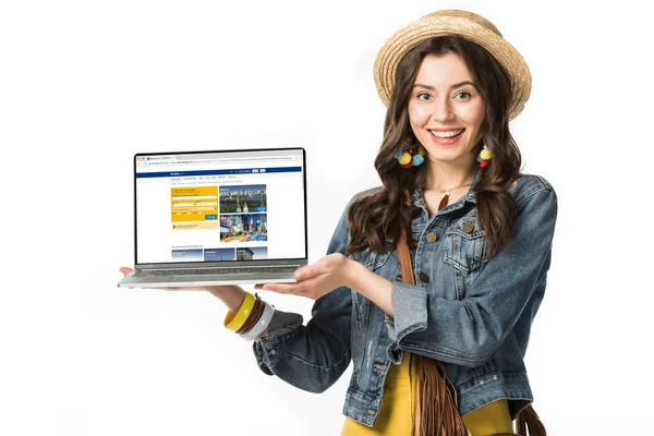 KYIV, UKRAINE - FEBRUARY 4, 2019: smiling hippie girl in straw hat holding laptop with booking website on screen isolated on white — Stock Photo