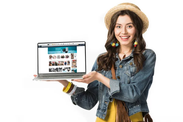 Kyiw, Ukraine - 4. Februar 2019: Lächelndes Hippie-Mädchen mit Strohhut hält Laptop mit Amazon-Website auf dem Bildschirm isoliert auf weiß — Stockfoto