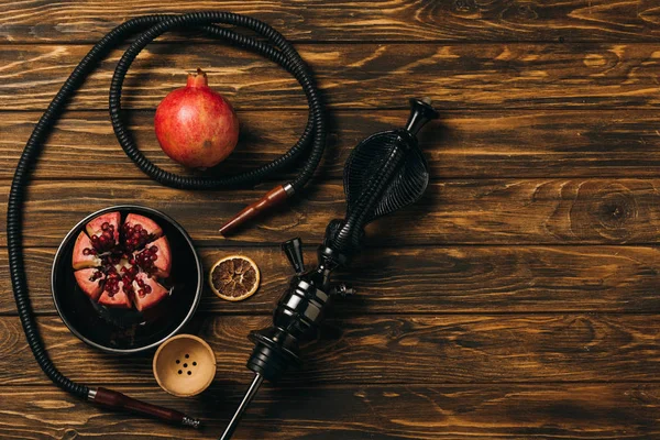 Top view of hookah, garnets and dried cut orange on wooden surface — Stock Photo