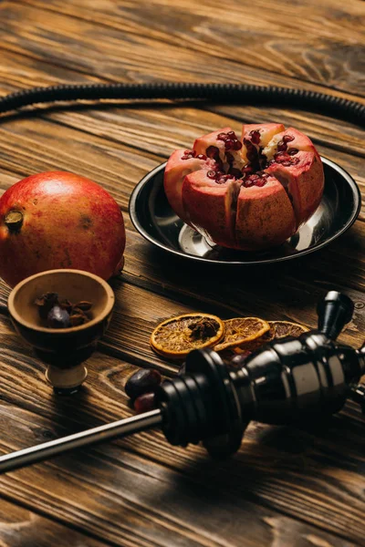 Hookah, garnets and dried cut oranges on wooden surface — Stock Photo