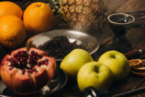 Narguilé, tabac, pommes, oranges, grenat et ananas sur la surface en bois — Photo de stock