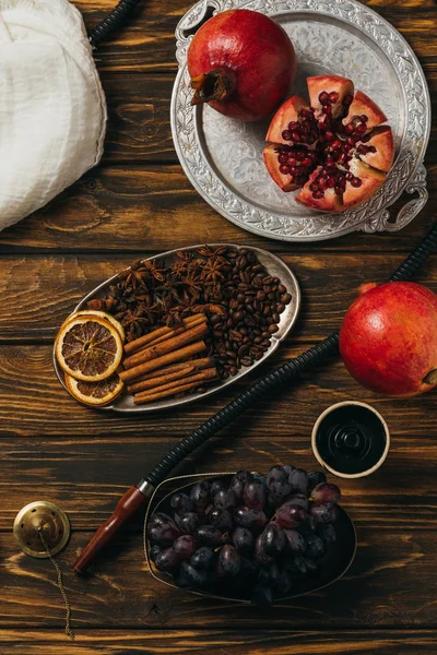 Top view of hookah, cinnamon, garnets, grapes and dried oranges on wooden surface — Stock Photo