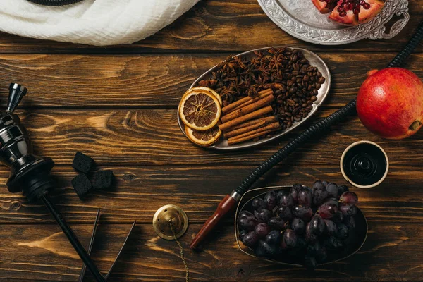 Vista superior de narguilé, canela, granadas, uvas, laranjas secas e carvões na superfície de madeira — Fotografia de Stock