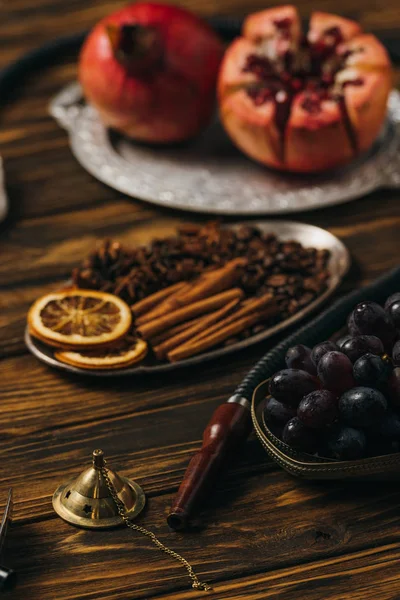 Foco seletivo de canela, granadas, uvas e narguilé na superfície de madeira — Fotografia de Stock